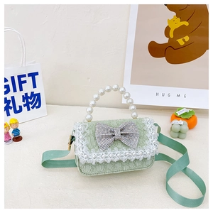 Macro view of green textured girl's bag with pearl handle and rhinestone bow details