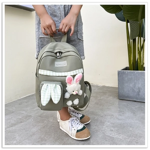 Detail of green kids backpack featuring a plush bunny and decorative checkered ribbon