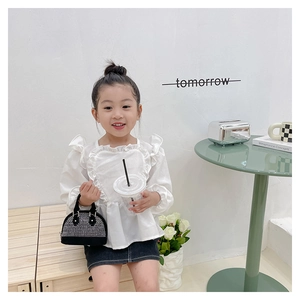 Detail of a girl wearing a white ruffled top and a black rhinestone mini handbag