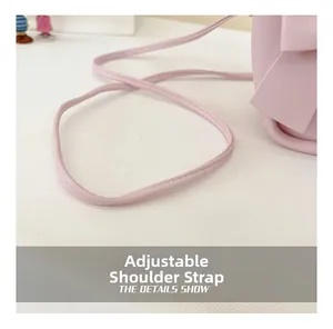 Detail view of adjustable shoulder strap and bow accent on pink PU leather handbag