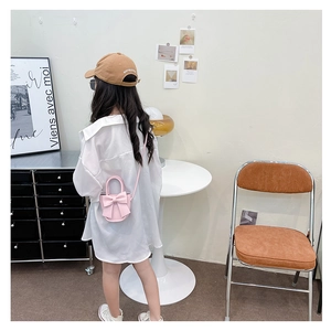Pink cute crossbody bag with 3D bow and handle worn by a child in a cozy setting