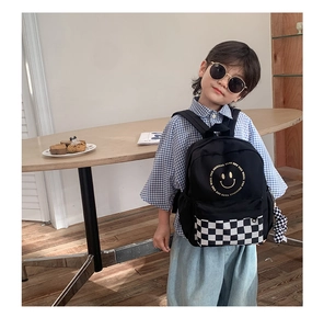 Kid modeling a black canvas backpack with a yellow smiley face and checkerboard pocket