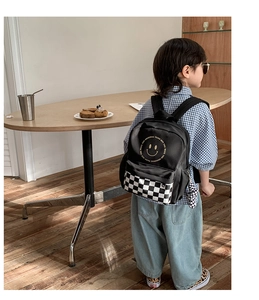 Detail of kids checkered backpack with yellow smiley face and plush bear charm