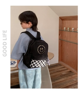 Detail view of smiley face kids backpack with checkered pocket worn by young model