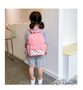 Pink kids backpack with smiley face and checkerboard pattern shown on a young model