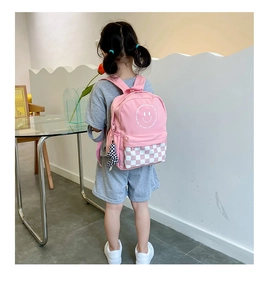 Pink kids backpack with smiley face and checkerboard pattern shown in use on back