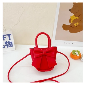 Detail of red PU leather child crossbody bag featuring large decorative bow and top handle