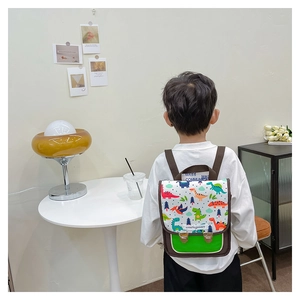 Detail eines Kindes mit weißem Rucksack mit bunten Dinosauriermotiven und grüner Tasche