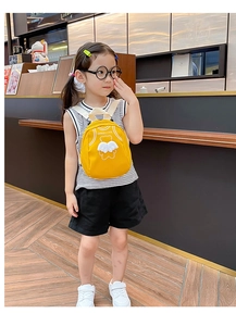 Toddler wearing yellow canvas backpack with white angel wings and Good Luck print