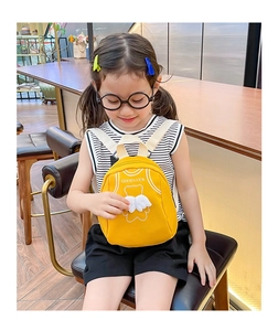 Detail of yellow toddler backpack with bear graphics worn by a child in a cozy indoor setting