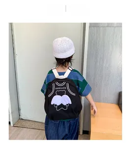 Detail view of children's black canvas backpack with cartoon bear and wings on a model