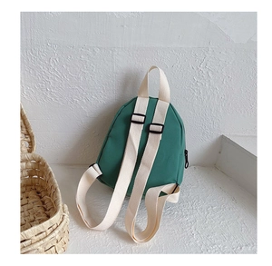Detail view of mini green canvas backpack showing adjustable cream straps and hand strap