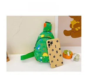 Detailed comparison of green cartoon dinosaur crossbody bag next to a mobile phone
