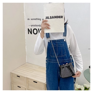 Detail of girl's mini bucket bag with rhinestones and silver chain on denim overalls