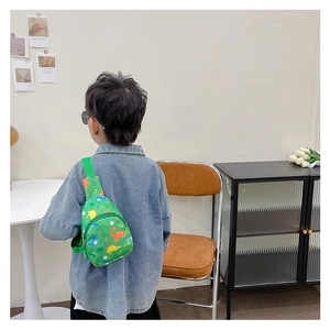 Detail of green kids crossbody bag with cute dinosaur prints worn by child on blue shirt