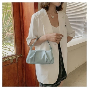 Close-up of mint green pleated cloud bag with slim handle worn over white blazer