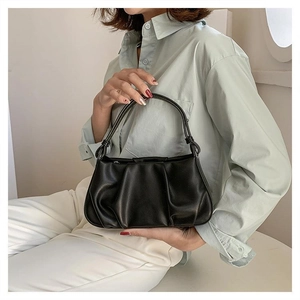 Detail of black ruched cloud bag with thin handles shown on elegant light blue outfit