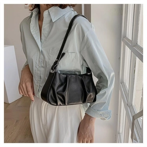 Detail of black pleated faux leather shoulder bag featuring adjustable metal buckle strap