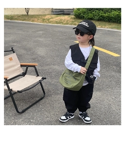 Outdoor street style view of a green canvas messenger bag with cool techwear vest