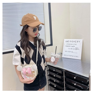 Fille portant un sac à bandoulière rond crème avec un nœud en paillettes roses et pochette
