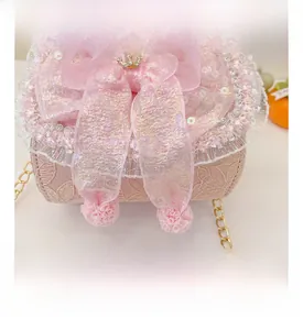 Close-up of pink lace handbag featuring a silk bow, gold crown, and metal chain strap