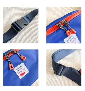 Detail of blue canvas kids fanny pack with orange zippers, buckle and woven logo patch