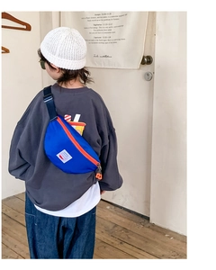 Detail view of a bright blue kids canvas chest bag with orange zipper on a young model