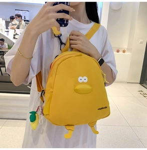 Detail of yellow cartoon duck backpack with plush legs and a cute lemon charm accessory