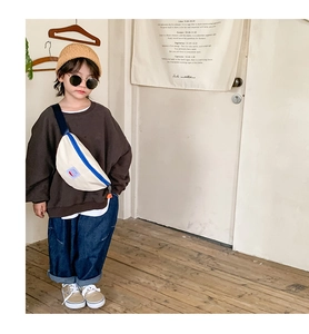 Kid carrying a beige canvas crossbody chest bag with blue zipper in a minimalist room