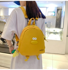 Detailed back view of a yellow cartoon duck backpack worn by a model in a bright mall