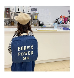 Detail of dark blue denim kids backpack with beige letter print in a casual store setting