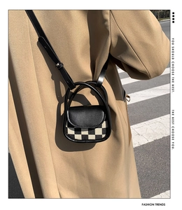 Close-up of mini checkered crossbody bag with black leather flap on trench coat