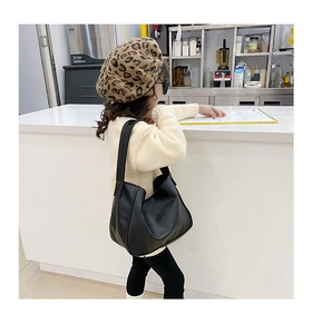 Detail view of a black faux leather hobo bag worn by a child model in a street style setting