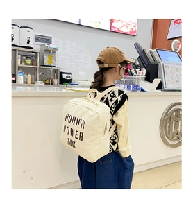 Detail view of cream canvas backpack with Brown Power MK print on wide shoulder strap