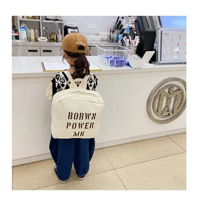 Detail of cream canvas toddler backpack featuring BORWN POWER MK letter print in a cafe setting