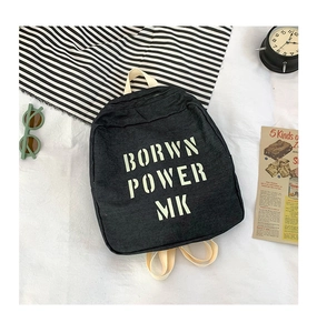 Flat-lay view of black denim backpack with white BORWN POWER MK lettering and accessories
