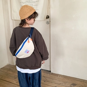 Kid's canvas chest bag in beige with blue zippers and orange pulls, worn by a child model