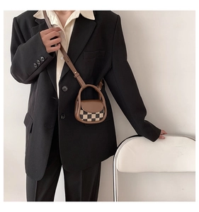 Close-up of a mini brown checkerboard crossbody bag on a model in a minimalist setting