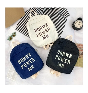 Detail of kids denim backpacks in cream, blue, and black with bold letter prints