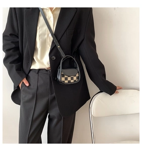 Mini plaid crossbody bag detail on a model wearing a black blazer in a minimalist setting