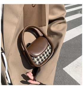 Detail of a mini houndstooth crossbody bag with chunky brown leather handle on a model