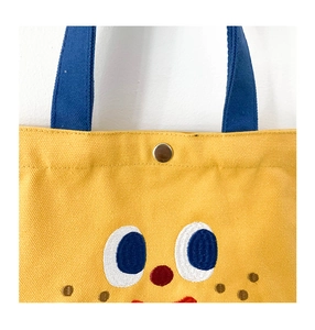 Close-up of yellow canvas tote bag with metal snap button and cute cartoon face embroidery