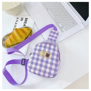 Détail du sac de poitrine enfant à carreaux mauves avec écusson ours sur un bureau
