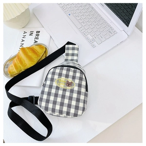 Détail du sac de poitrine à carreaux pour enfants avec écusson ours sur un bureau épuré