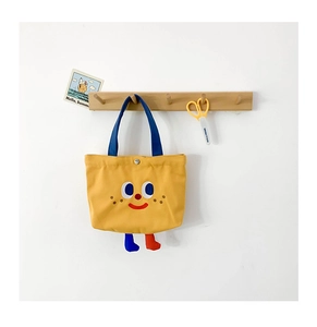 Detail of yellow canvas handbag with embroidered cartoon smile and blue handles