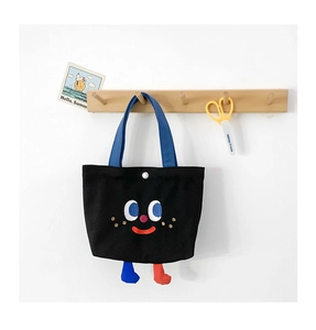 Detail of black canvas tote with cartoon face embroidery and 3D plush feet accents