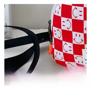 Détail du sac de poitrine enfant à damier rouge avec imprimés smiley et tirette orange