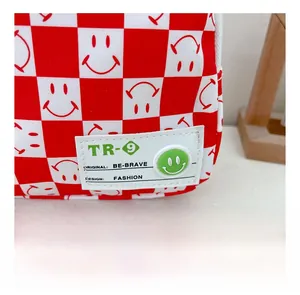 Détail du sac enfant à damier rouge avec patch smiley et bouton décoratif vert