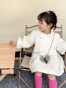 Detail of white long sleeve girl's dress with ruffled chest and textured fabric