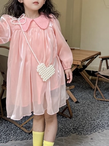 Detail of pink long-sleeved girls' dress with heart-shaped pearl bag and bow necklace